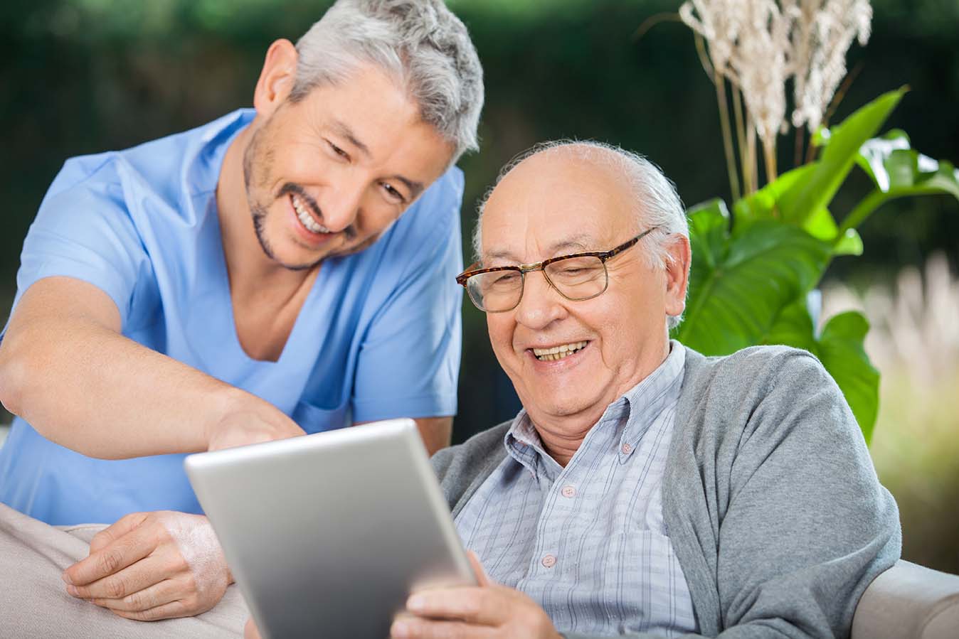 Happy male nurse and senior man enjoying while using tablet